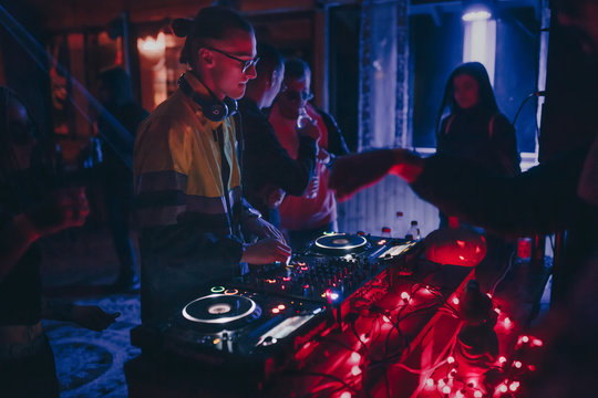 Chisinau, Moldova 11.10.2019. Rave techno DJ plays concert set with CD player turn table & Pioneer sound mixer surrounded by dancing people crowd minimal tracks party mix