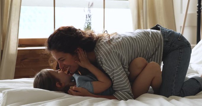 Carefree mum and kid daughter having fun playing on bed