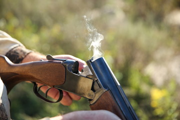 smoking rifle in hunter's hands close up. hunter's hand takes out a cartridge from a smoking gun