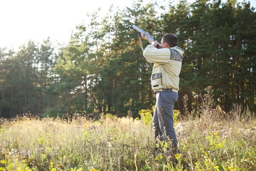 hunter full length aiming a hunting rifle up in the forest in summer