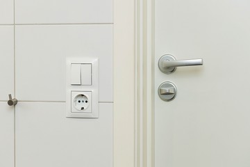 Close up view of power socket and power switch near door handle on white wall and door. Interior design elements concept. 