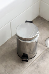 Metal silver garbage can with lid on the floor in the hotel bathroom with white tiles  on the wall. Bathroom modern luxury interior 