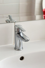 Silver metal shiny faucet water switch and ceramic sink with big mirror on background in hotel home spa bathroom with white tiles on wall. Bathroom luxury interior. Soft selective blurred focus 