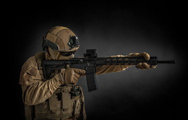 Modern soldier in full ammunition with weapons in his hands on a black background. The military aims from an automatic rifle.
