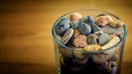 Small sea stones in a glass vessel. The idea of decorating the house with small rocks in a jar on a wooden blurred background.