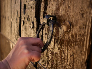 Female hand knocks on a round metal beater on a wooden old door