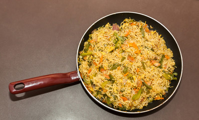 Top view of egg noodles in a non stick frying pan on a table with brown background