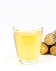 Sugarcane juice in glass and pile of sugarcane beside isolated on white background.