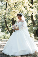 Fototapeta na wymiar Bride holding a bouquet of flowers. Beautiful woman. Wedding bouquet in bride's hands. Beautiful bride in white dress in the park. Beautiful woman with professional make up and hair style.