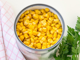 Canned sweet corn in a tin can and parsley on a table. Side dish and ingredient for salads. Vegetarian food.