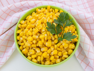 Canned sweet corn in a green bowl near checkered kitchen towel on a table. Side dish and ingredient for salads. Vegetarian.