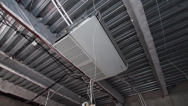 Air conditioner on the ceiling in the room under construction. Wires are hanging from ceiling