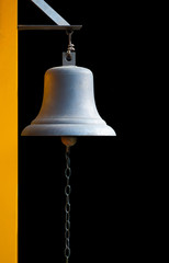 An old bell hang on yellow pole with black background. It can use for alarm or warning. It can use in many cases like fire alarm, classroom break, signal at train station and temple and others.