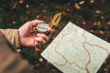 A man holds a compass and a paper map in his hand and is guided by the area, autumn forest,...
