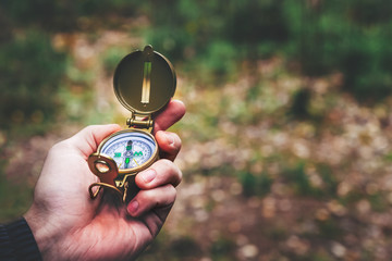 A man holds a compass and a paper map in his hand and is guided by the area, autumn forest,...