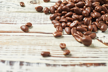 One heap of many tasty dragees chocolate coated peanuts scattered on old worn white rustic wooden table. Space for text. Close-up