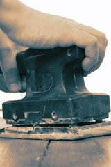 Man sanding wooden floor with an electric sander.  With colour toning