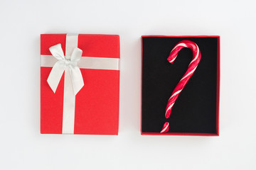 Red Christmas present box with question mark from candy cane on white background. Gift choice concept. Top view, flat lay, copy space