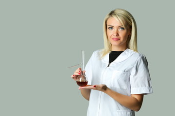 laboratory assistant in a white coat holds a flask with liquid on gray background.