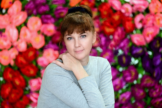 Close-up portrait of an adult woman with red hair on a colored background in a gray sweater in the studio. Clean face skin, age-related cosmetics.