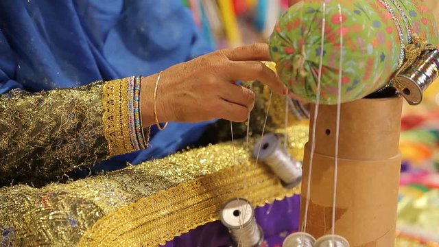 Arab women in traditional costumes sew national costumes. With large spools of thread. Multi-colored bright fabrics. Large round spindle in the hands of one of the women. Just hands