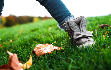 Cute children's legs in jeans and boots with bunnies in the green grass with autumn leaves