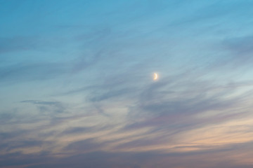 Sunset sky with gray clouds and crescent moon.
