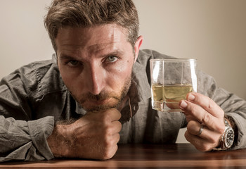 alcoholic depressed and wasted addict man sitting in front of whiskey glass trying holding on drinking in dramatic expression suffering alcoholism and alcohol addiction