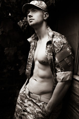 Portrait of attractive male soldier wearing camouflage uniform with open jacket revealing pecs and...