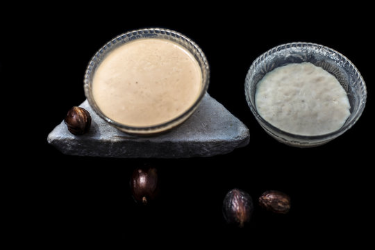 Nutmeg spice face mask on black surface consisting of some curd well mixed with nutmeg or jaifal powder in a glass bowl.Shot with raw spice and curd.Horizontal top shot.
