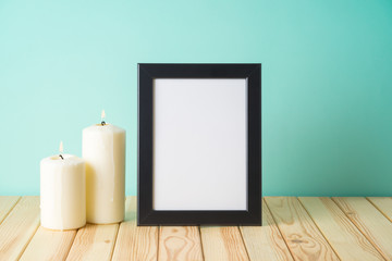 Photo frame mockup and candles on wooden table over blue background