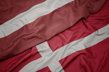 waving colorful flag of denmark and national flag of latvia.