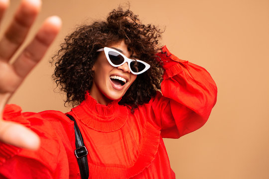 Fototapeta Portrait of beautiful young black woman taking selfie.Portrait of a pretty young afro american woman in retro style clothes smiling while standing and taking a selfie isolated over beige.