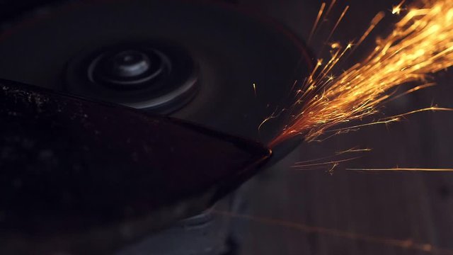 Man sharpening axe with grinder in the dark with flying sparks. Slow motion