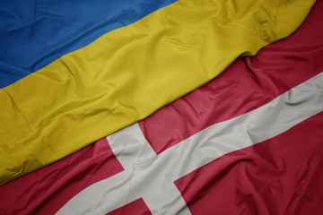 waving colorful flag of denmark and national flag of ukraine.