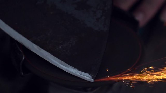 Man sharpening axe with grinder in the dark with flying sparks. Slow motion