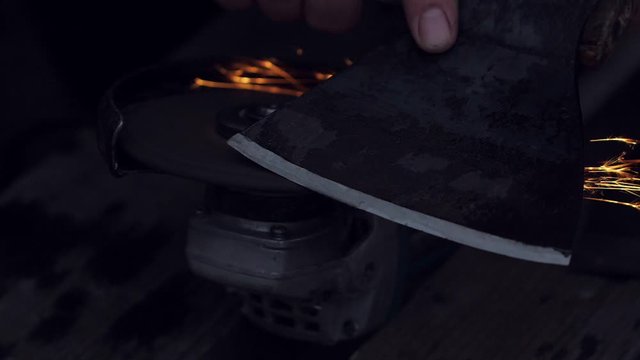 Man sharpening axe with grinder in the dark with flying sparks. Slow motion