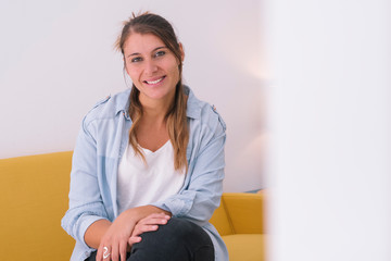 Cheerful young woman with white copy space. She is a young entrepreneur. Portrait of an isolated caucasian woman on a yellow couch. Young strong woman at a start up. Co working modern lifestyle. 
