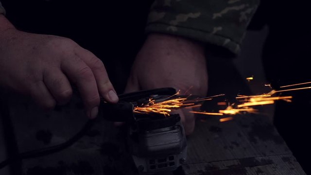Man sharpening axe with grinder in the dark with flying sparks. Slow motion