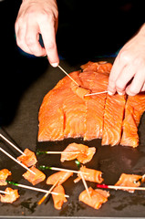 Top, front view, close distance of two hands rolling  slices of smoked salmon and pierced with a...
