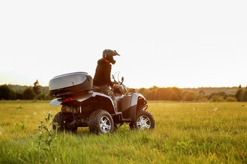 a man in a black helmet rides an ATV across a field at sunset. © Petr Smagin