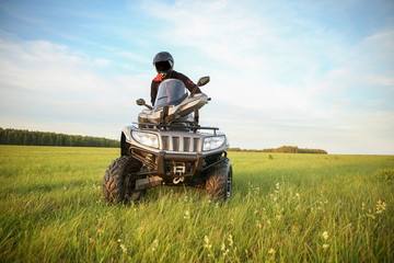 a man in a black helmet rides an ATV across a field at sunset.