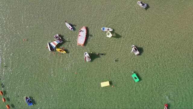 Top down aerial footage of People on various colourful floating Mats and small boats at the Beach.
