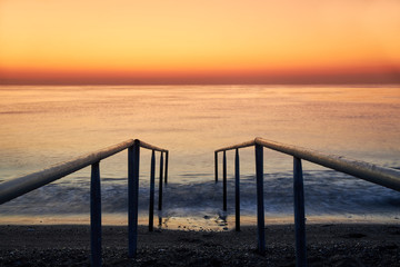 Fototapeta premium Ladder to enter the sea on the beach and a beautiful sunrise at sea