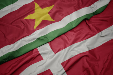 waving colorful flag of denmark and national flag of suriname.