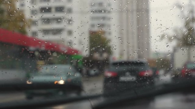 Driving a car in the rain autumn day view through the windshield raindrops, defocused cinematic effect