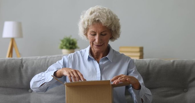 Happy old senior woman open parcel in living room