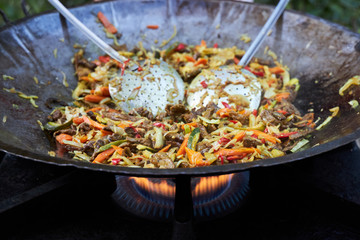 Delicious homemade wok is cooked in a large frying pan on a gas stove.