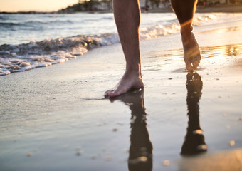 Male feet walking on the beach during sunset, close-up