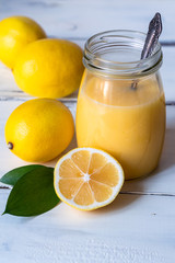 lemon curd in a jar and lemons on white background